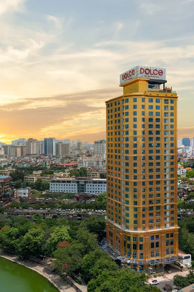 A guest swimming in a 24K gold-tiled infinity pool at Dolce by Wyndham Hanoi Golden Lake with the city skyline reflecting on the water.