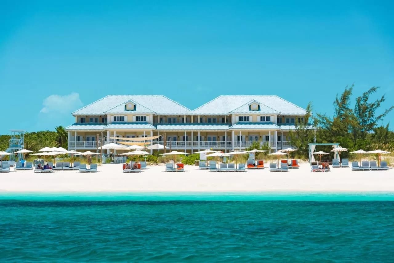 A private 'Pampering Pod' on Grace Bay Beach with white linens and turquoise water in the background.