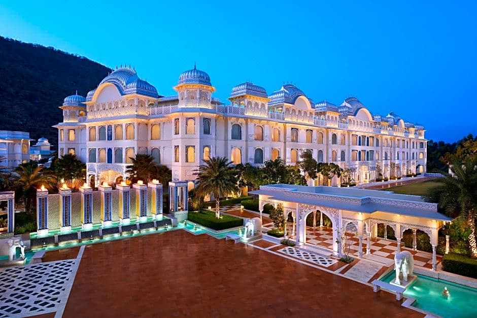 The white marble facade of The Leela Palace Jaipur illuminated at dusk, featuring silver domes and the reflection pool.