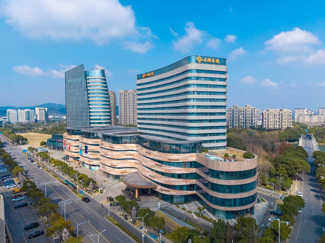 A serene, symmetrical view of the Suzhou Shihu Lake Jinling Garden Hotel exterior at dusk, reflecting traditional Song Dynasty architectural elements onto the calm waters of Xiaoshi Lake.
