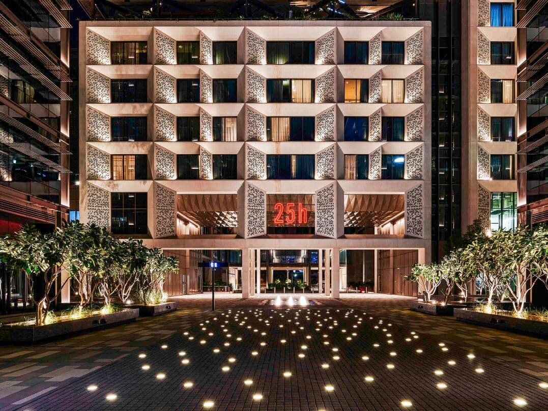 A low-angle shot of the Monkey Bar terrace at night, featuring lush greenery and rattan furniture, with the illuminated calligraphy of the Museum of the Future dominating the background.