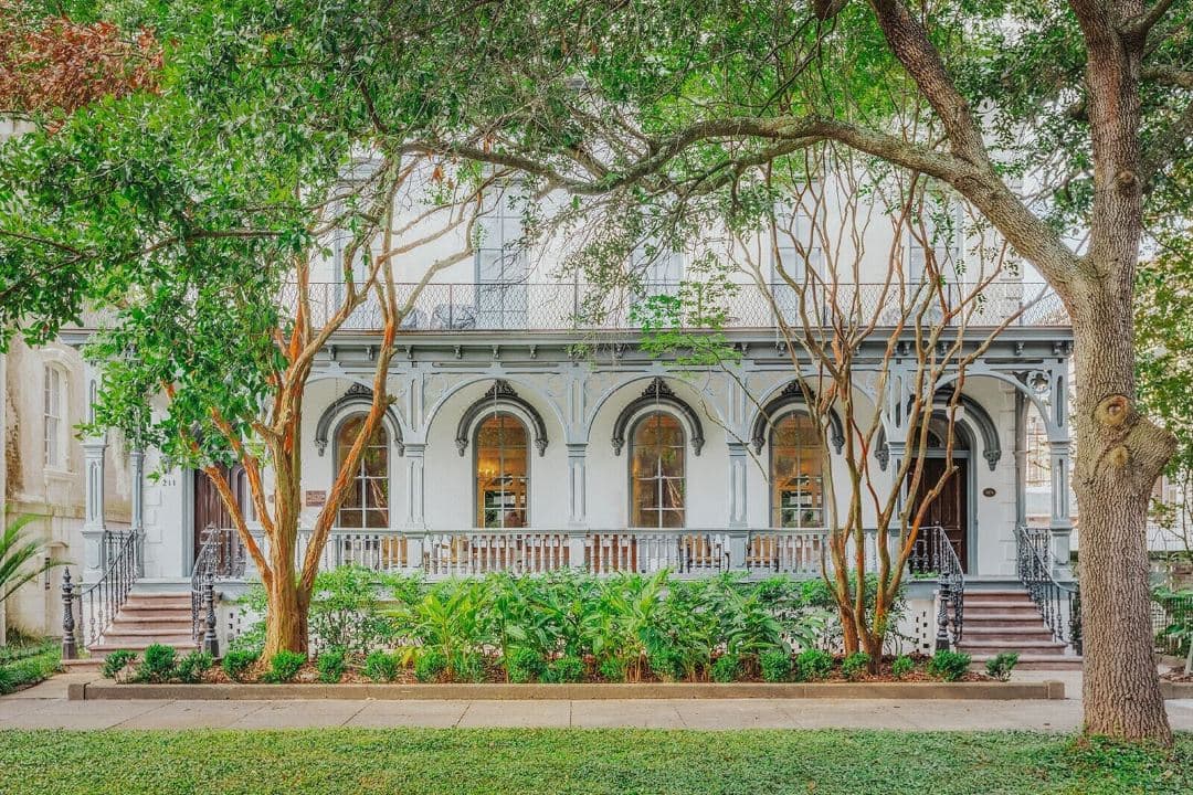 A moody, low-lit courtyard at Bellwether House featuring guests holding champagne flutes during the sunset sabrage ritual, surrounded by lush greenery and wrought-iron details.