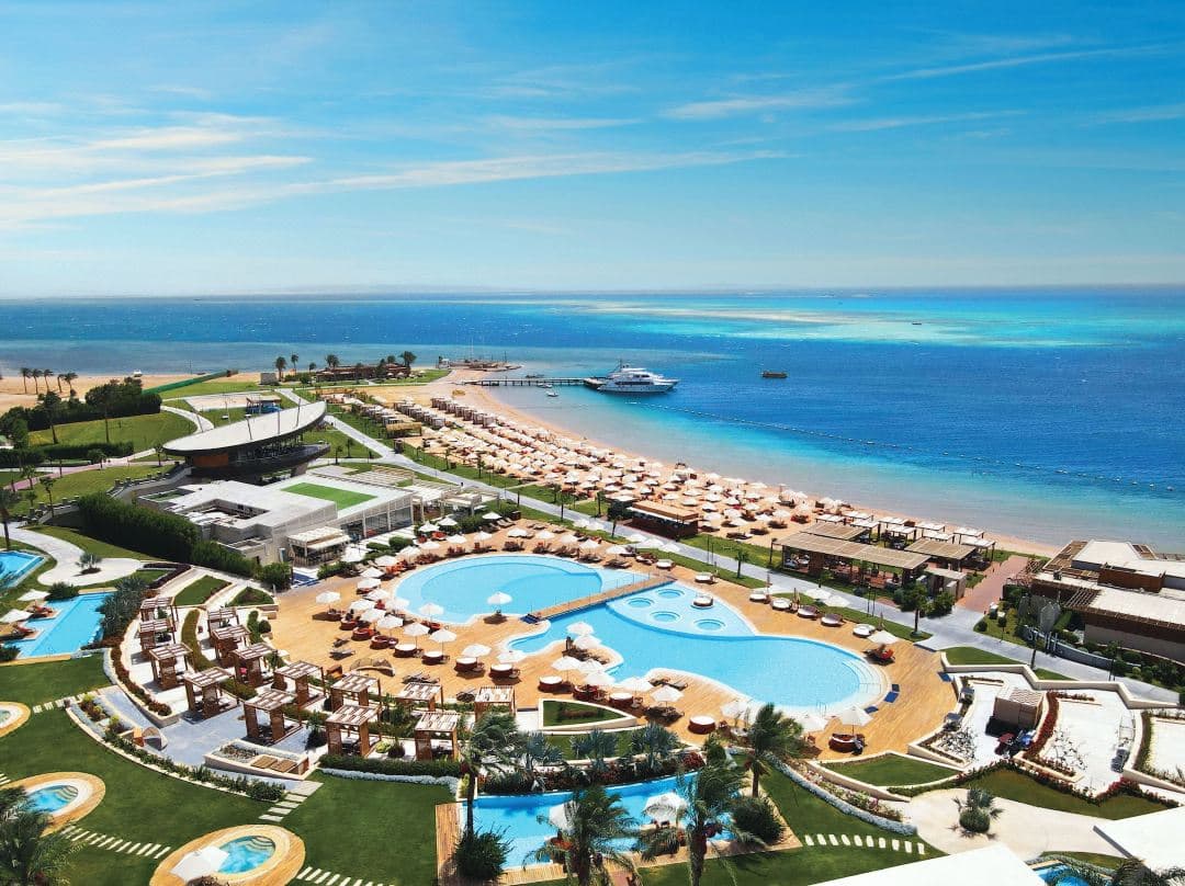 A kitesurfer gliding across the flat turquoise lagoon at Rixos Premium Magawish, with modern swim-up villas visible in the background.