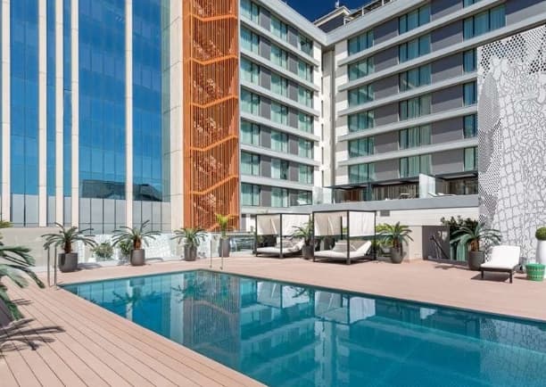 Rooftop pool deck at Barceló Imagine featuring a seasonal plunge pool and sun loungers with the inclined KIO Towers in the background.