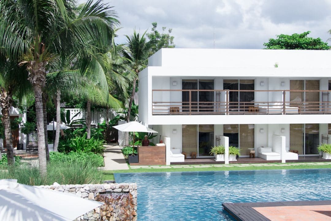 Minimalist white sun loungers lining the Silksand pool at Putahracsa Hua Hin, framed by mature heritage trees and geometric architecture.