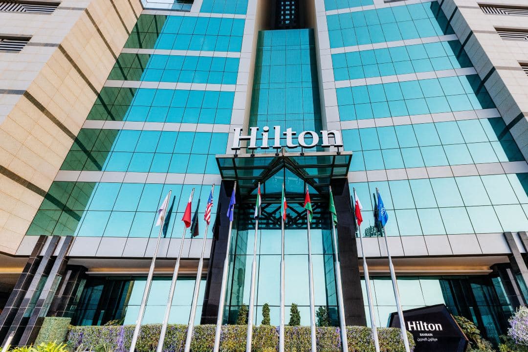 The illuminated 45-story tower of Hilton Bahrain reflecting on the water at twilight, dominating the Juffair skyline.