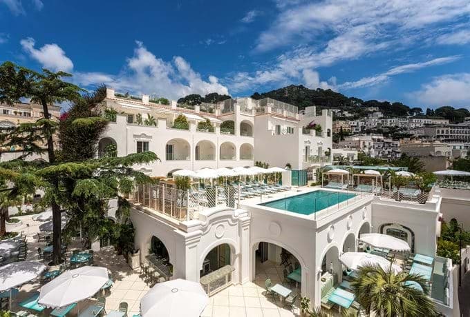 The whitewashed facade of Hotel La Palma Capri featuring arched windows and wrought-iron balconies under a bright blue sky.