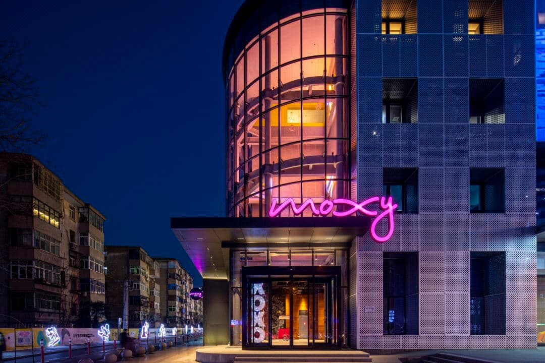 Vibrant Moxy Xi'an Beilin lobby featuring modern design, a lively bar, and a welcoming front desk for international guests.