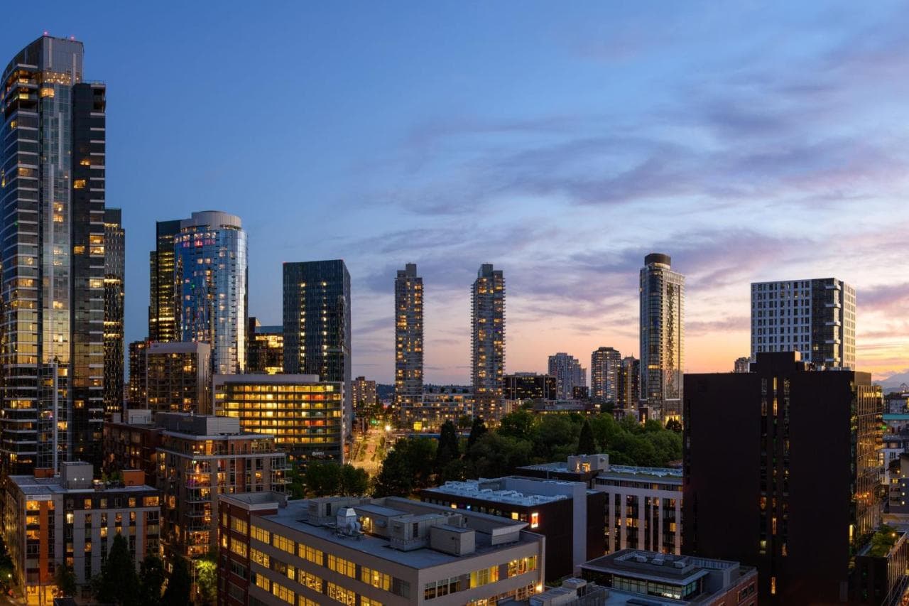A sleek, modern rooftop bar at sunset featuring fire pits and a dramatic, close-up view of the Space Needle against the Seattle skyline.