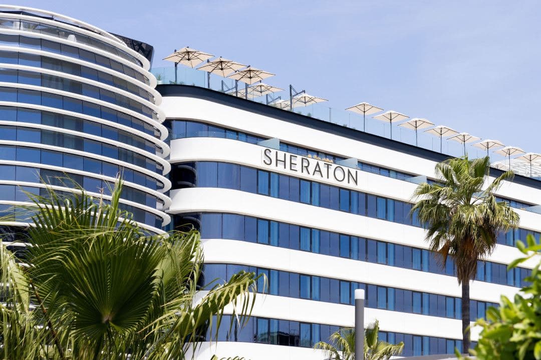 A sleek rooftop pool at Sheraton Nice Airport with a commercial airplane taking off in the background against a sunset sky.