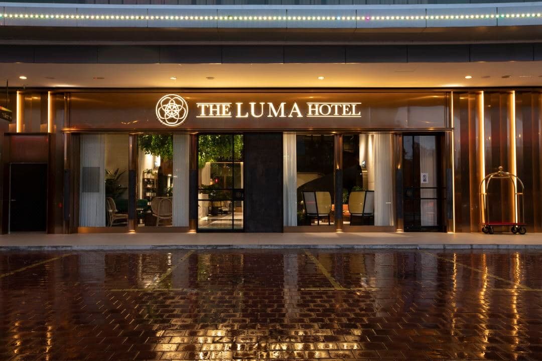 Top-down view of The Luma Hotel's signature wooden spiral staircase surrounded by indoor tropical plants in the lobby.