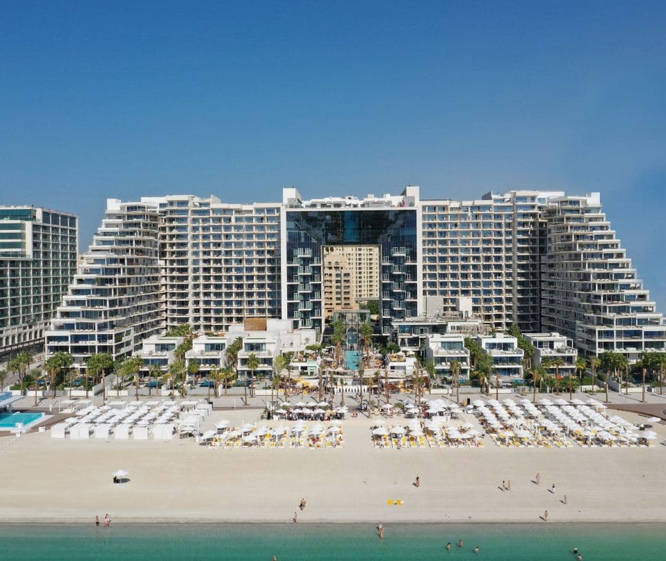 The iconic glass cube entrance of FIVE Palm Jumeirah framing the central Social Pool and Dubai Marina skyline at sunset.