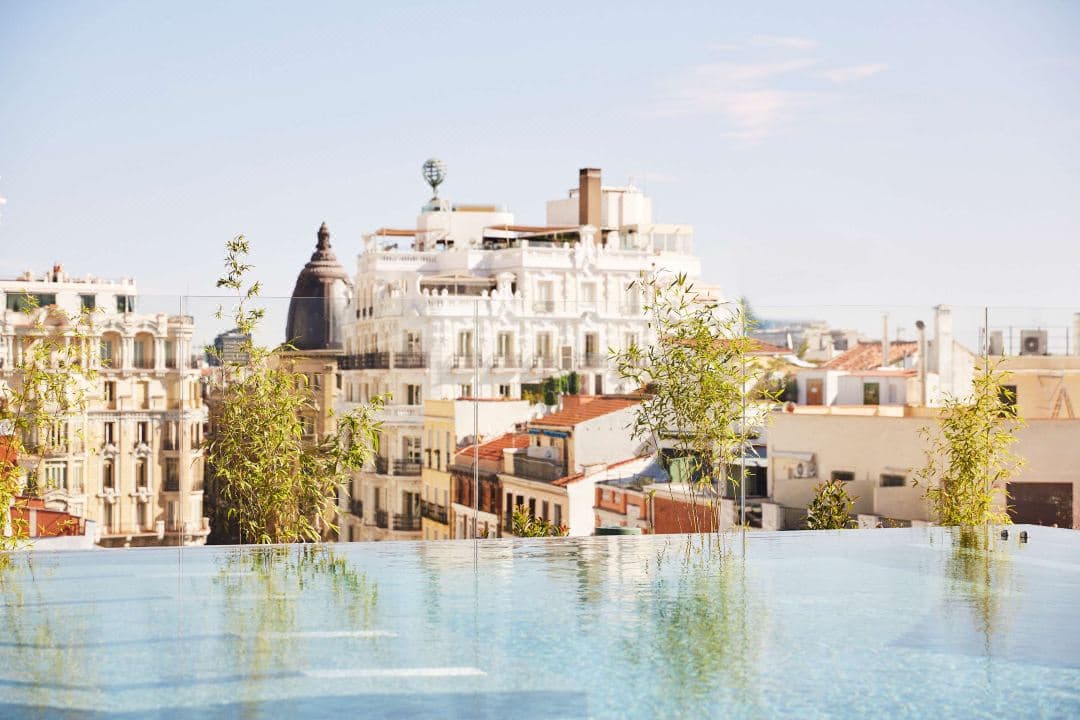A moody, mid-century modern rooftop terrace at Thompson Madrid featuring an infinity dipping pool and guests enjoying cocktails against a backdrop of the Madrid skyline and the Telefónica building.