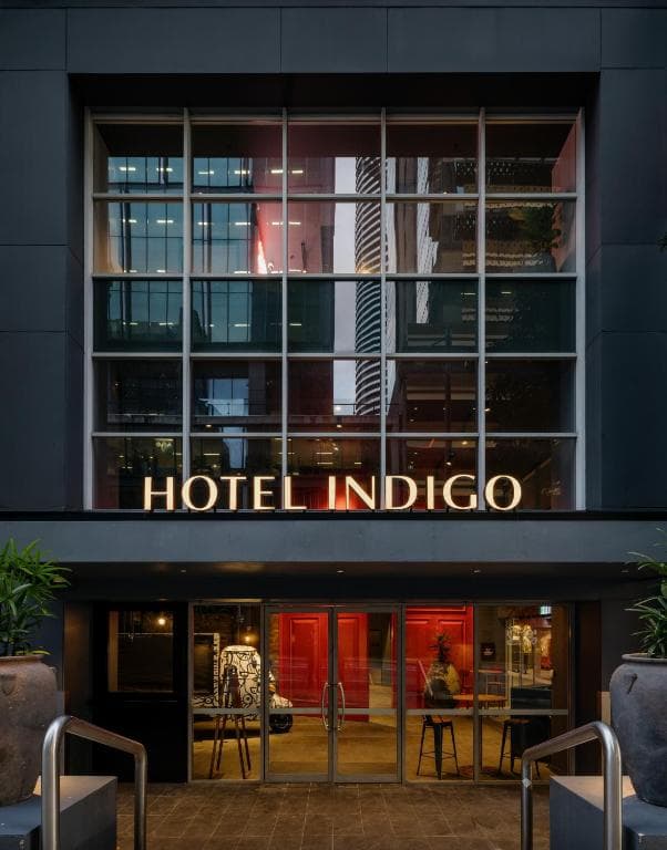 Oversized red timber entrance doors at Hotel Indigo Brisbane, opening into an industrial-chic lobby with graffiti murals.