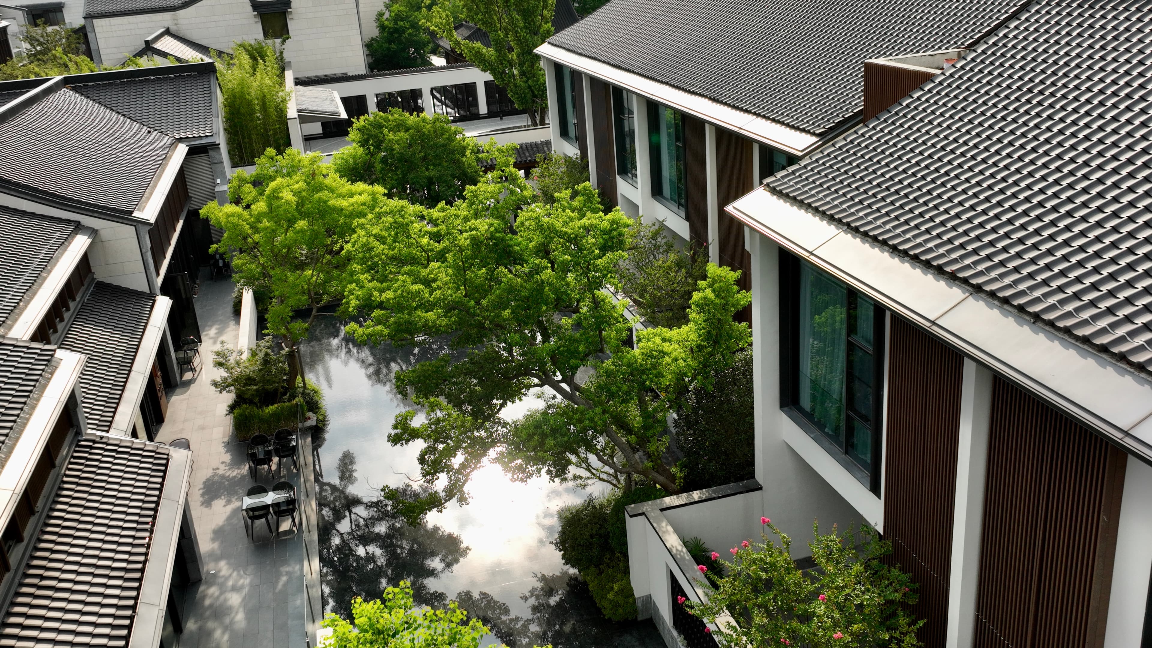 Reflections of whitewashed pavilion walls and black tiled roofs in the serene central water courtyard of Kimpton Bamboo Grove Suzhou.