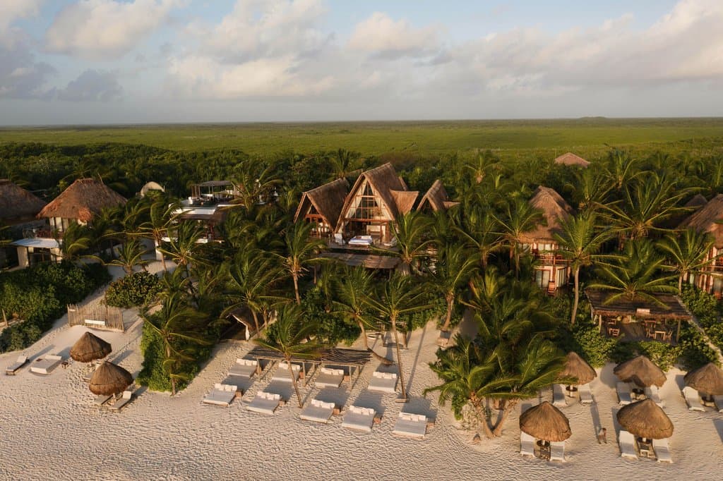 King-sized bed rolled out onto a wooden terrace overlooking the turquoise Caribbean sea, framed by a thatched palapa roof at La Valise Tulum.