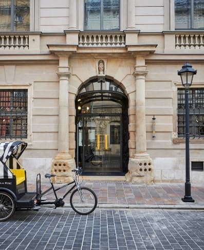 The glass-roofed Orangery at Artesse restaurant, featuring modern furniture set against historic palace walls.