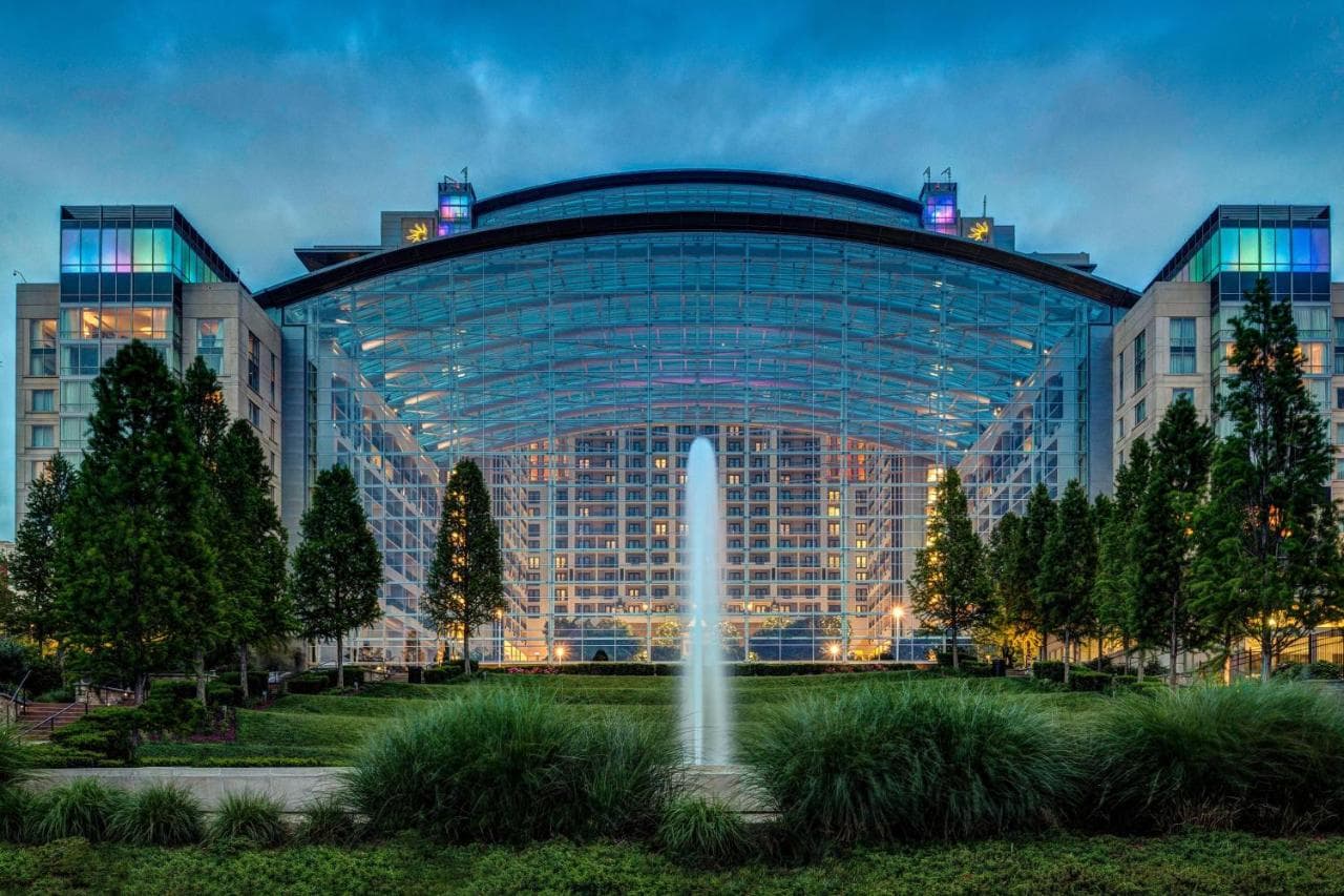 The massive 19-story glass atrium of Gaylord National Resort illuminated at night, featuring indoor gardens and the colonial-style village facades.