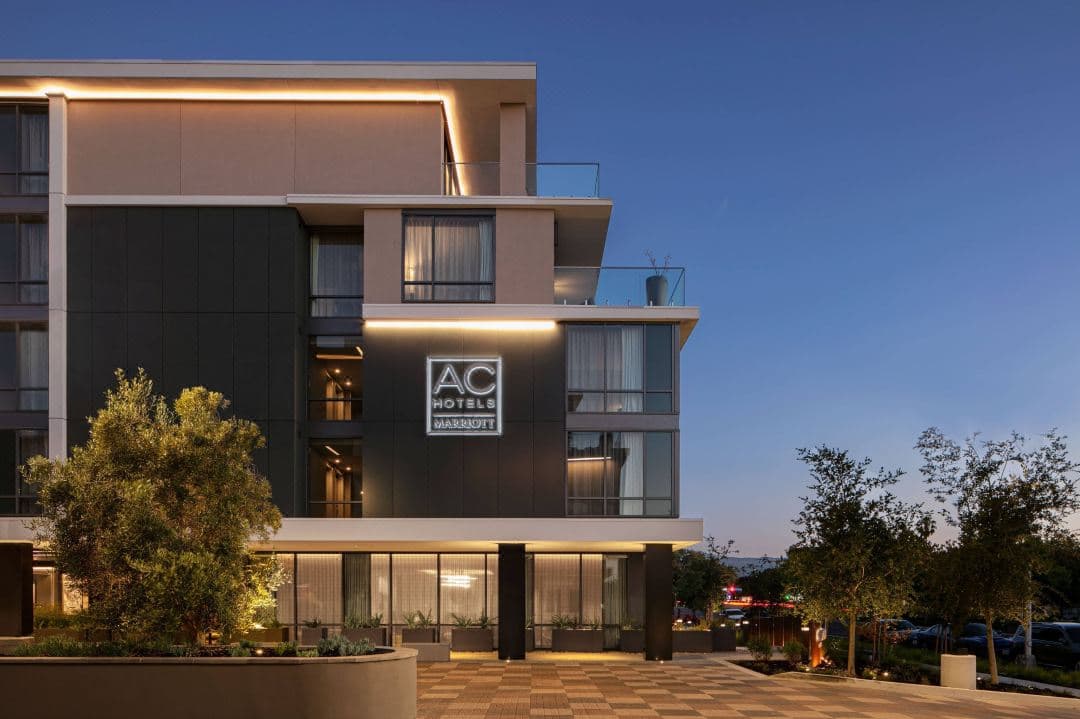 The AC Hotel Palo Alto courtyard at dusk featuring modern pergolas, comfortable seating, and a linear fire feature illuminating the minimalist facade.