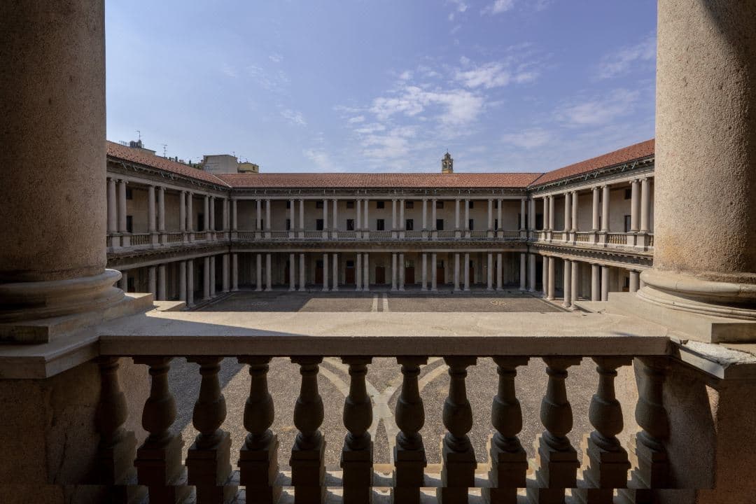 The monumental baroque colonnade of Portrait Milano's Piazza del Quadrilatero, illuminated at twilight with guests dining at outdoor tables.