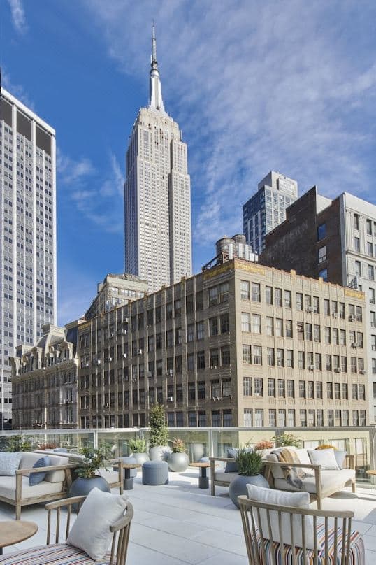 A guest lounging at the Virgin Hotels NYC outdoor pool with the Empire State Building towering directly overhead.