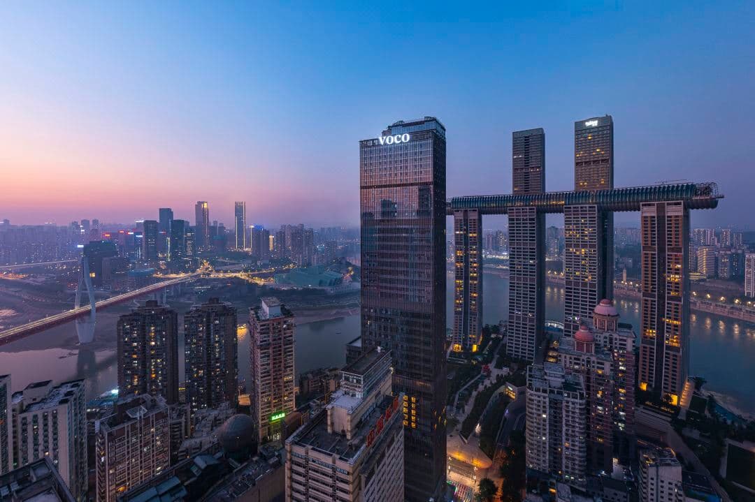 View from voco Chongqing 12th floor terrace looking up at the curved Raffles City Crystal skybridge at twilight.