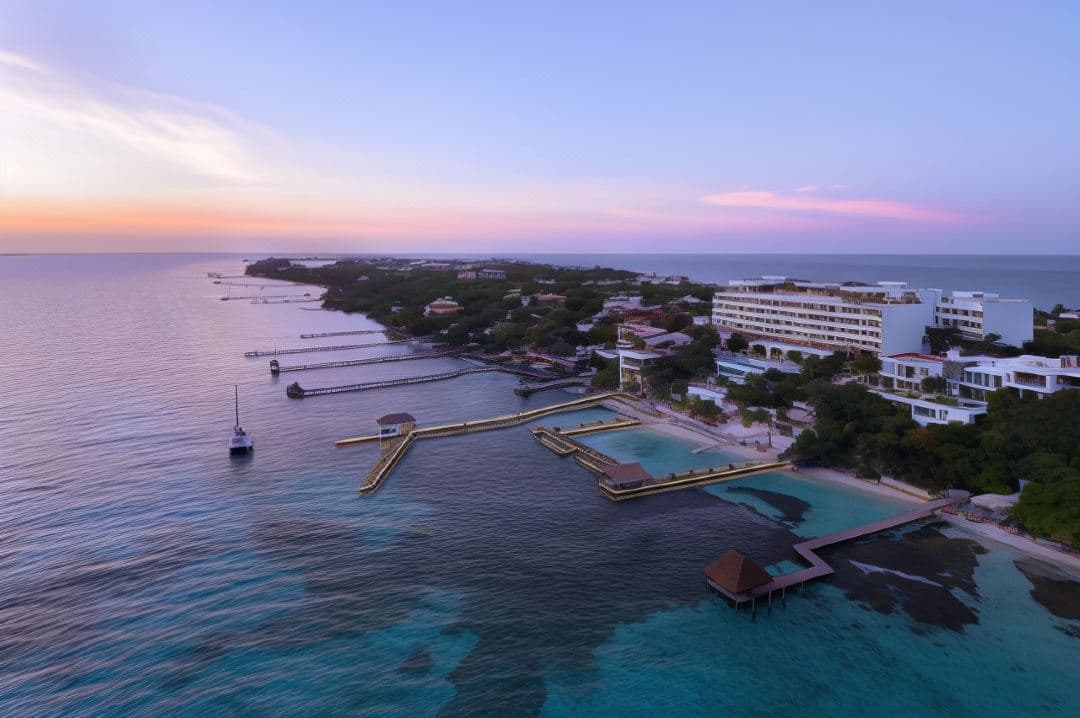 A woman in a white sun hat relaxing in the UNIK rooftop infinity pool at Impression Isla Mujeres, overlooking the turquoise Caribbean sea at sunset.