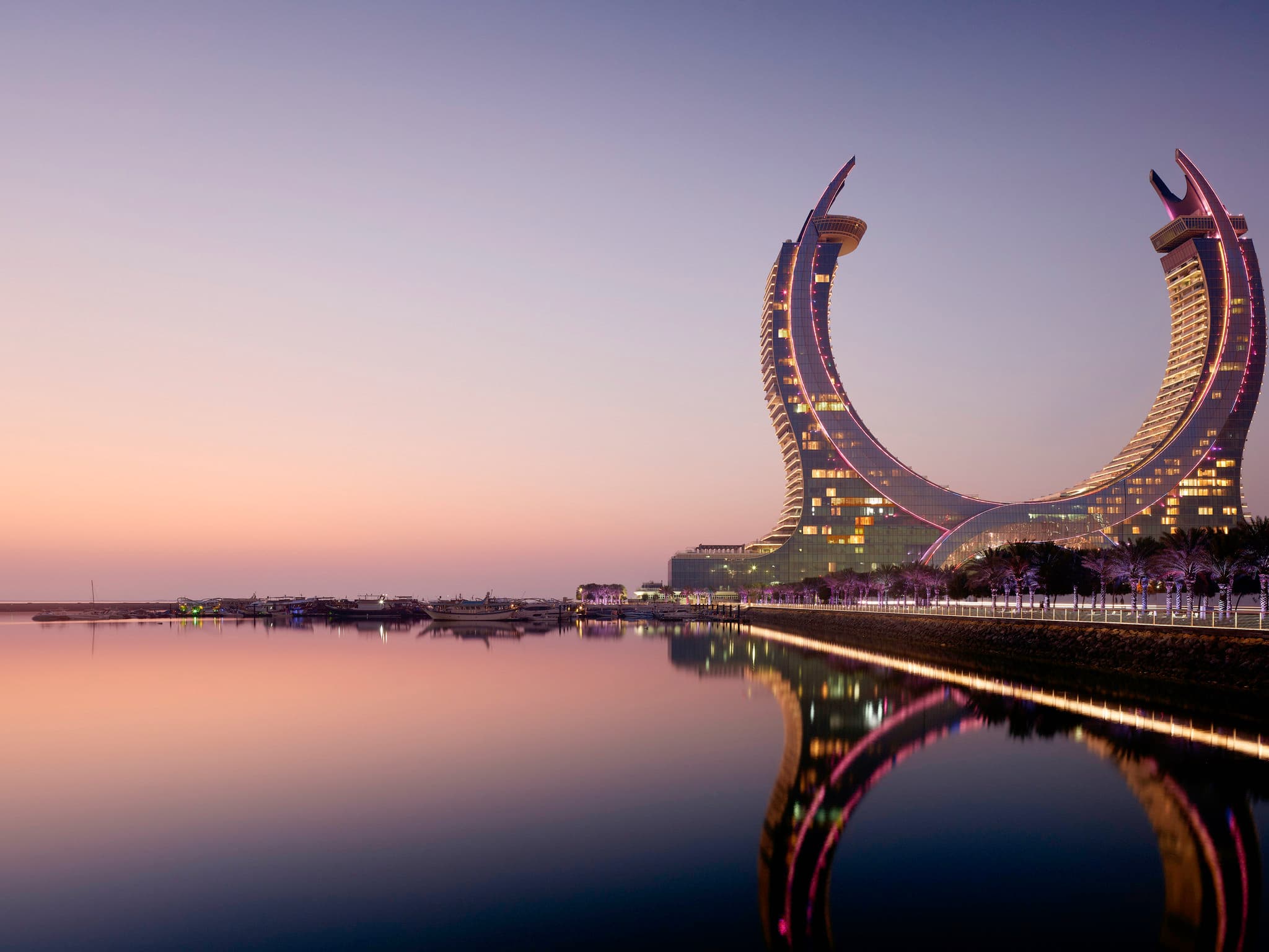 The soaring, kaleidoscopic atrium of Raffles Doha featuring cloud projections and intricate white architectural curves.