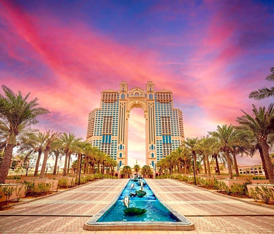 The iconic illuminated arch of Rixos Marina Abu Dhabi reflecting over the adult pool at twilight.