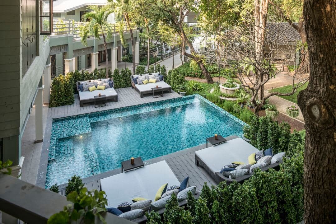 The 120-year-old Banyan tree shading the swimming pool at The Raweekanlaya Bangkok, surrounded by white colonial architecture.