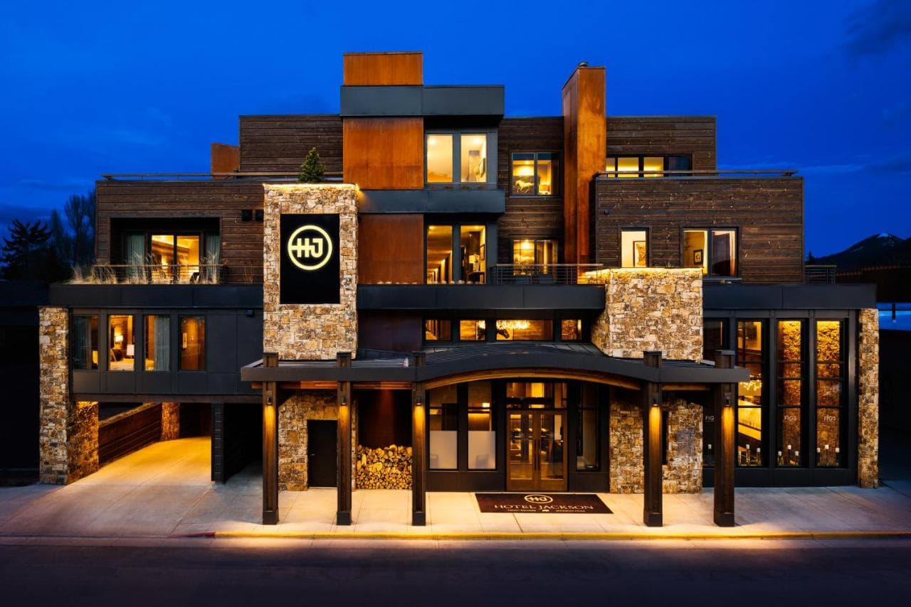 Hotel Jackson exterior at dusk featuring modern rustic architecture with warm lighting and Snow King Mountain in the background.
