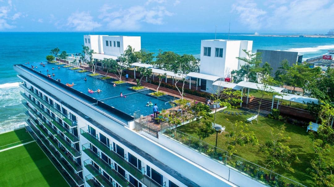 Expansive 60-meter rooftop infinity pool at Marino Beach Colombo with guests looking out over the Indian Ocean at sunset.