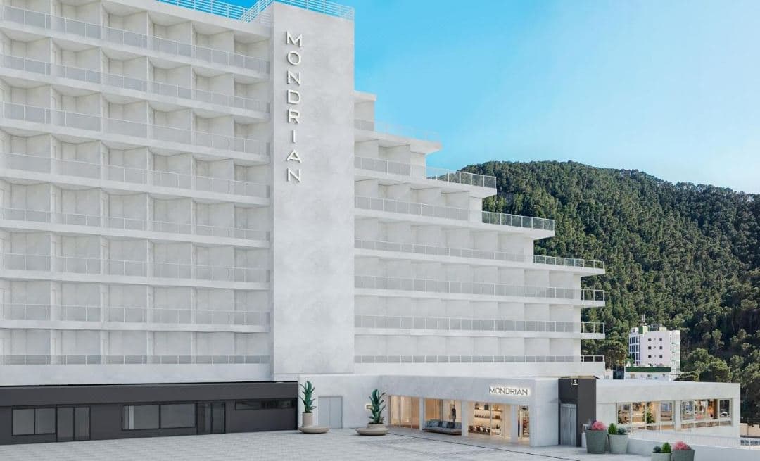 从伊比萨Mondrian酒店阳台俯瞰Cala Llonga海湾的绿松石色海水,周围环绕着松树。