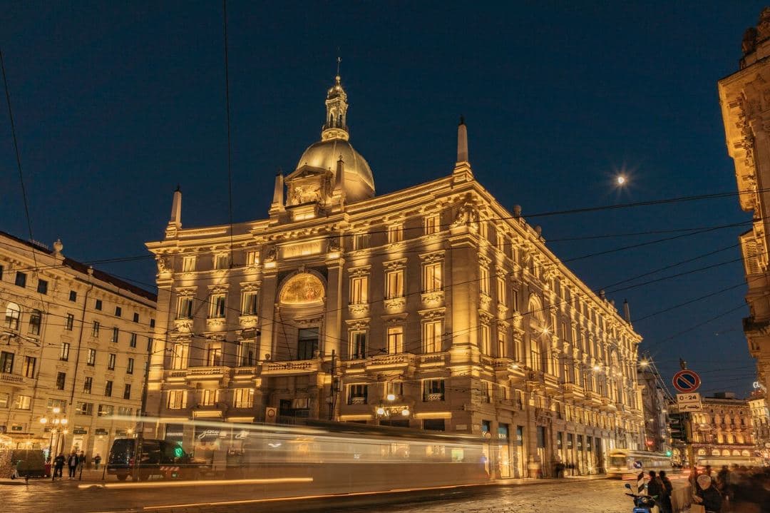 The illuminated neo-medieval façade of Palazzo Cordusio Gran Meliá at twilight, featuring the signature copper dome and arched windows.