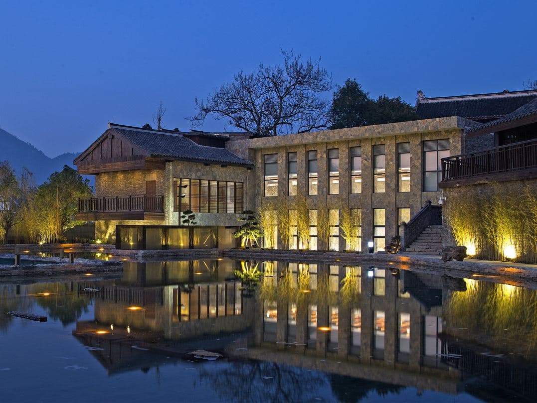 A serene central courtyard at VEN Courtyard Guiyang featuring grey stone Tunpu architecture, a reflective water pool, and traditional wooden columns under soft lighting.
