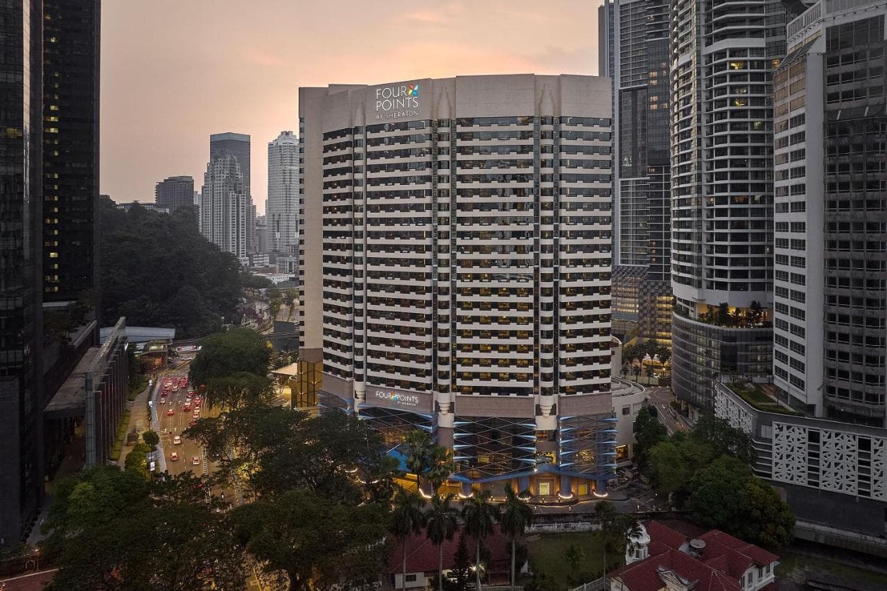 A massive outdoor pool deck in Kuala Lumpur featuring water slides and sun loungers, with the Petronas Twin Towers visible in the background.
