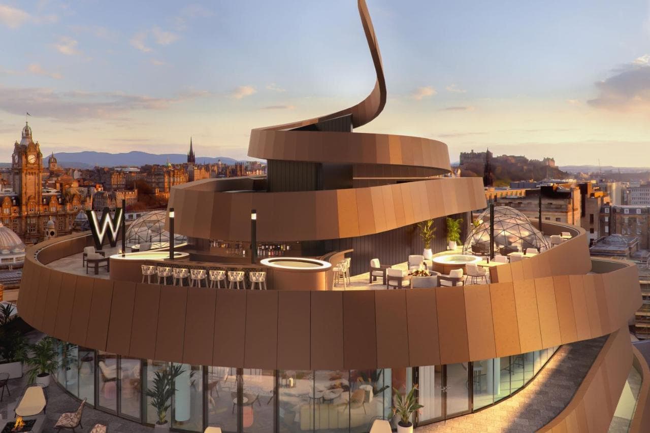The bronze ribbon façade of W Edinburgh glowing at dusk against the historic city skyline.