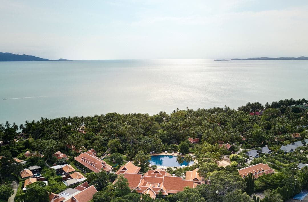 Aerial view of Santiburi Koh Samui's massive 50m circular pool surrounded by red umbrellas and lush tropical gardens.