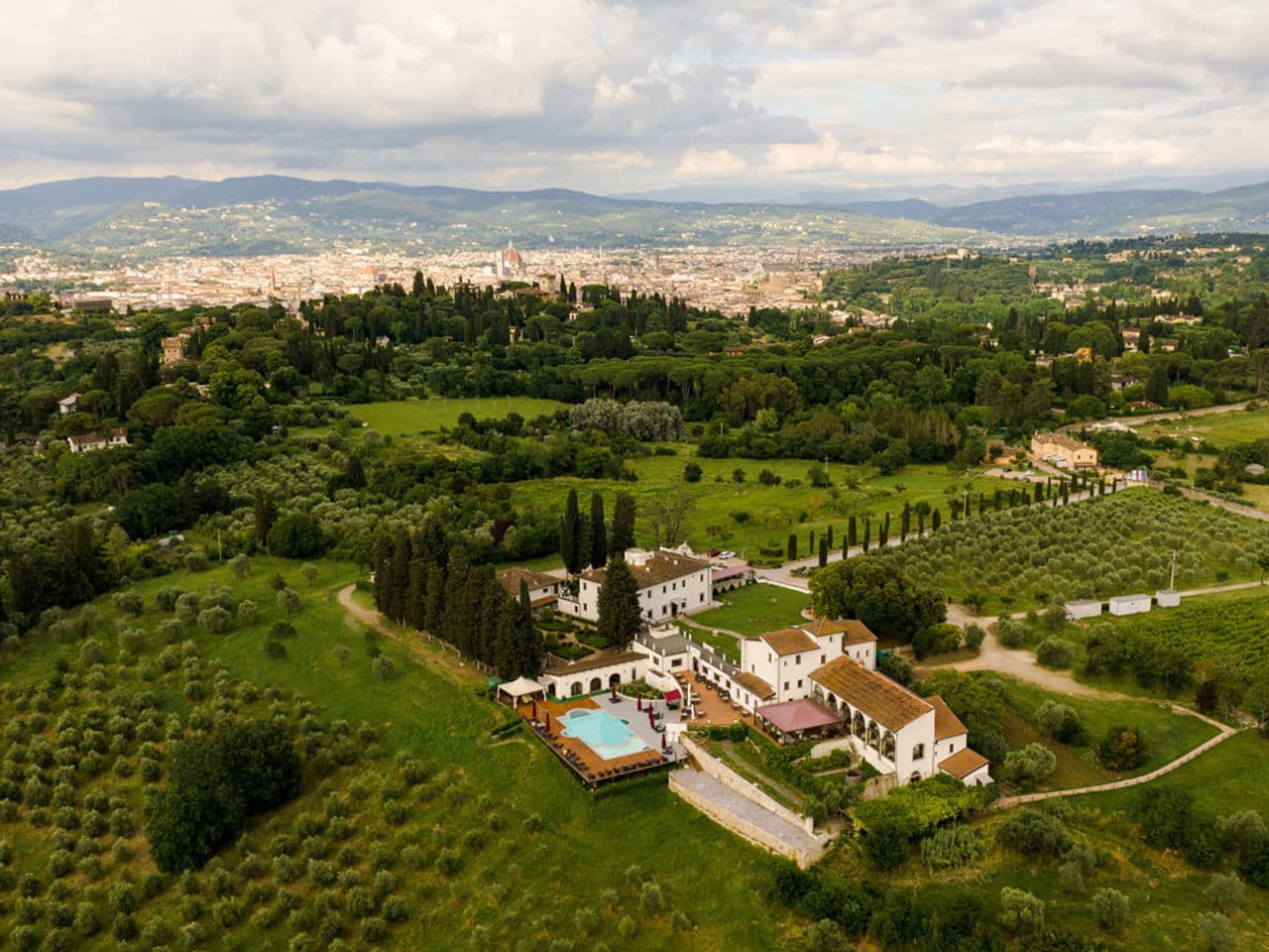 A heated infinity pool at Villa Tolomei overlooking the terracotta rooftops of Florence and the Tuscan hills at sunset.