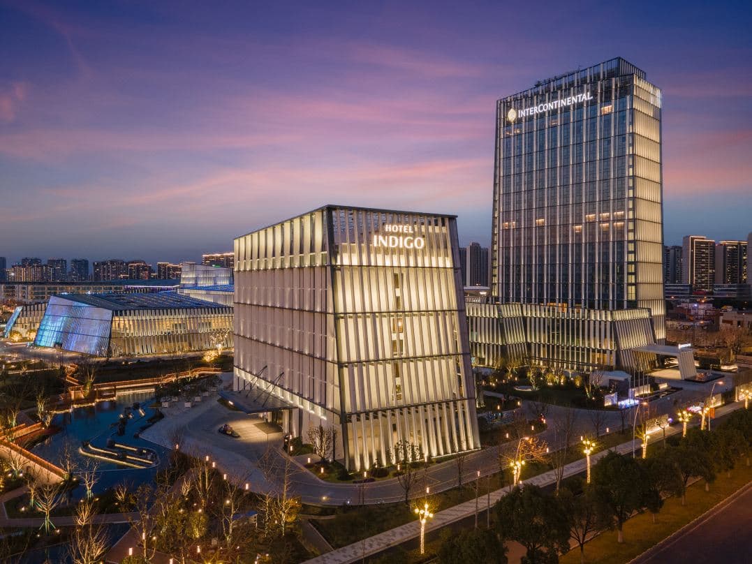 A sleek rooftop swimming pool at Hotel Indigo Wuxi with a backdrop of blue skies and the distant silhouette of Xuntang Ancient Town.