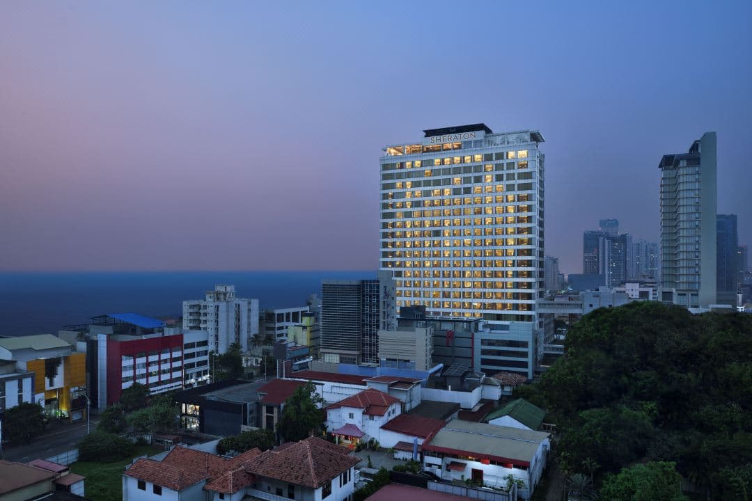 A sleek rooftop infinity pool at Sheraton Colombo at dusk, reflecting the illuminated city skyline and the deep blue Indian Ocean.