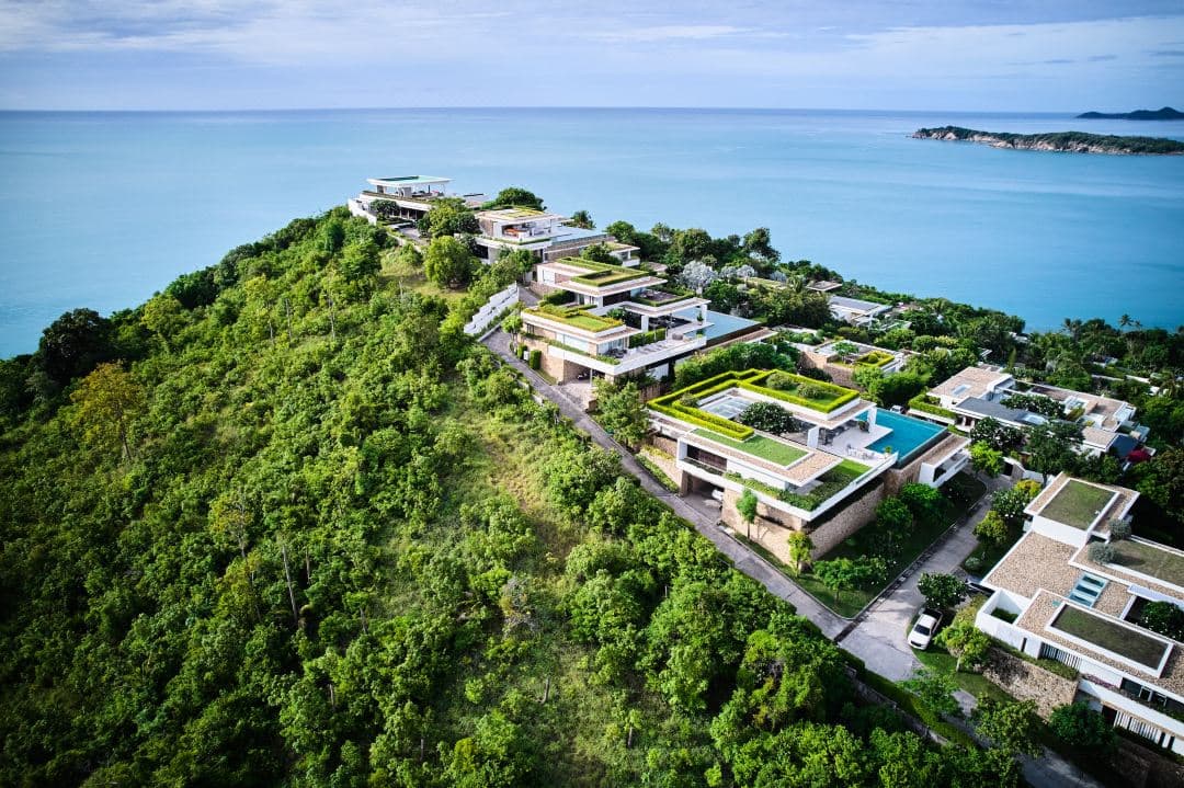 A massive concrete brutalist villa at Samujana Ko Samui with a saltwater infinity pool weaving around natural rock boulders overlooking the Gulf of Thailand.
