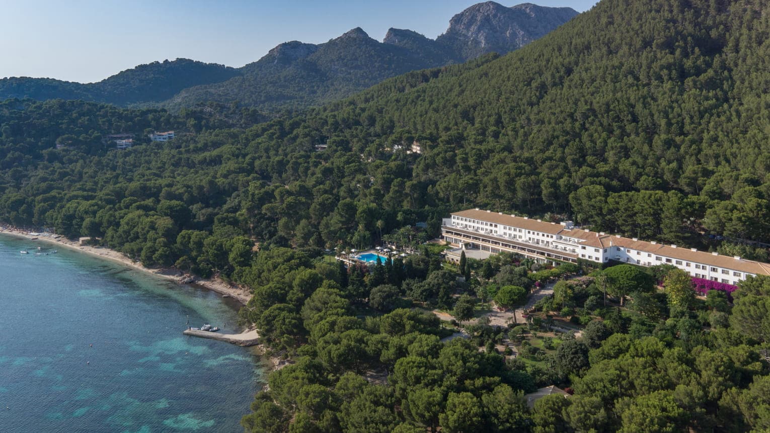 A guest looks out from a limestone balcony at the Four Seasons Mallorca, framed by Aleppo pines and the turquoise Formentor bay.