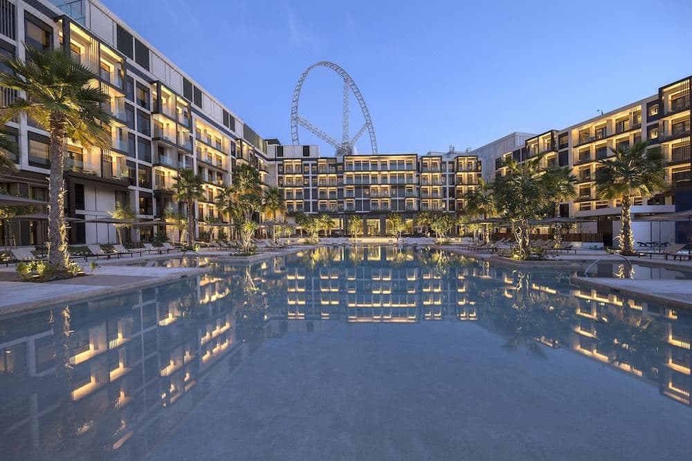 The iconic Delano Dubai swimming pool featuring canary yellow umbrellas, sunken furniture, and minimalist white architecture under a blue sky.