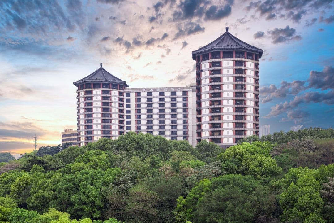 A stately mid-century hotel balcony overlooking a lush hillside and the traditional Chinese architecture of Yuejiang Tower in the distance.