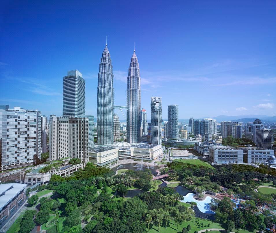 A dramatic dusk shot from inside the SkyBar at Traders Hotel Kuala Lumpur, featuring the illuminated saltwater pool in the foreground and the Petronas Twin Towers filling the floor-to-ceiling windows in the background.