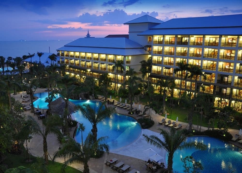 Expansive free-form lagoon pool at Ravindra Beach Resort bordered by palm trees and traditional Thai pavilions at sunset.