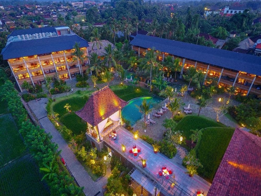 Alaya Resort Ubud main pool surrounded by green rice paddies and palm trees at sunrise.