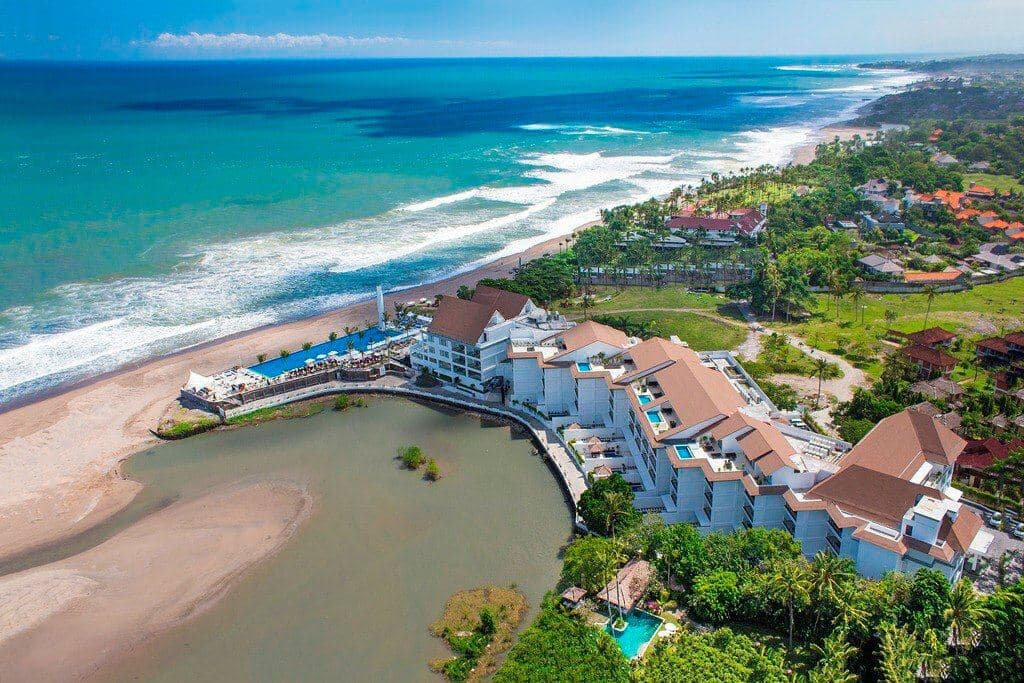 A dramatic 50-meter infinity pool at Lv8 Resort Hotel stretching towards the Berawa coastline at sunset, framed by white colonial-style architecture.
