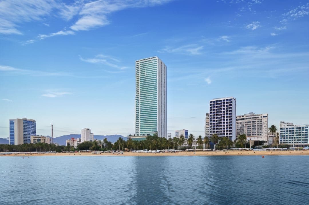 A guest silhouette sitting against a floor-to-ceiling glass wall at Muong Thanh Luxury Nha Trang, overlooking the vast blue ocean and Vinpearl Land in the distance.